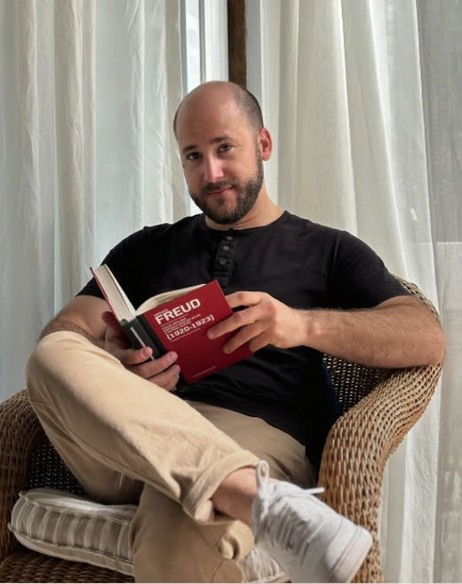 Natanael Jotar sentado em uma poltrona com um livro